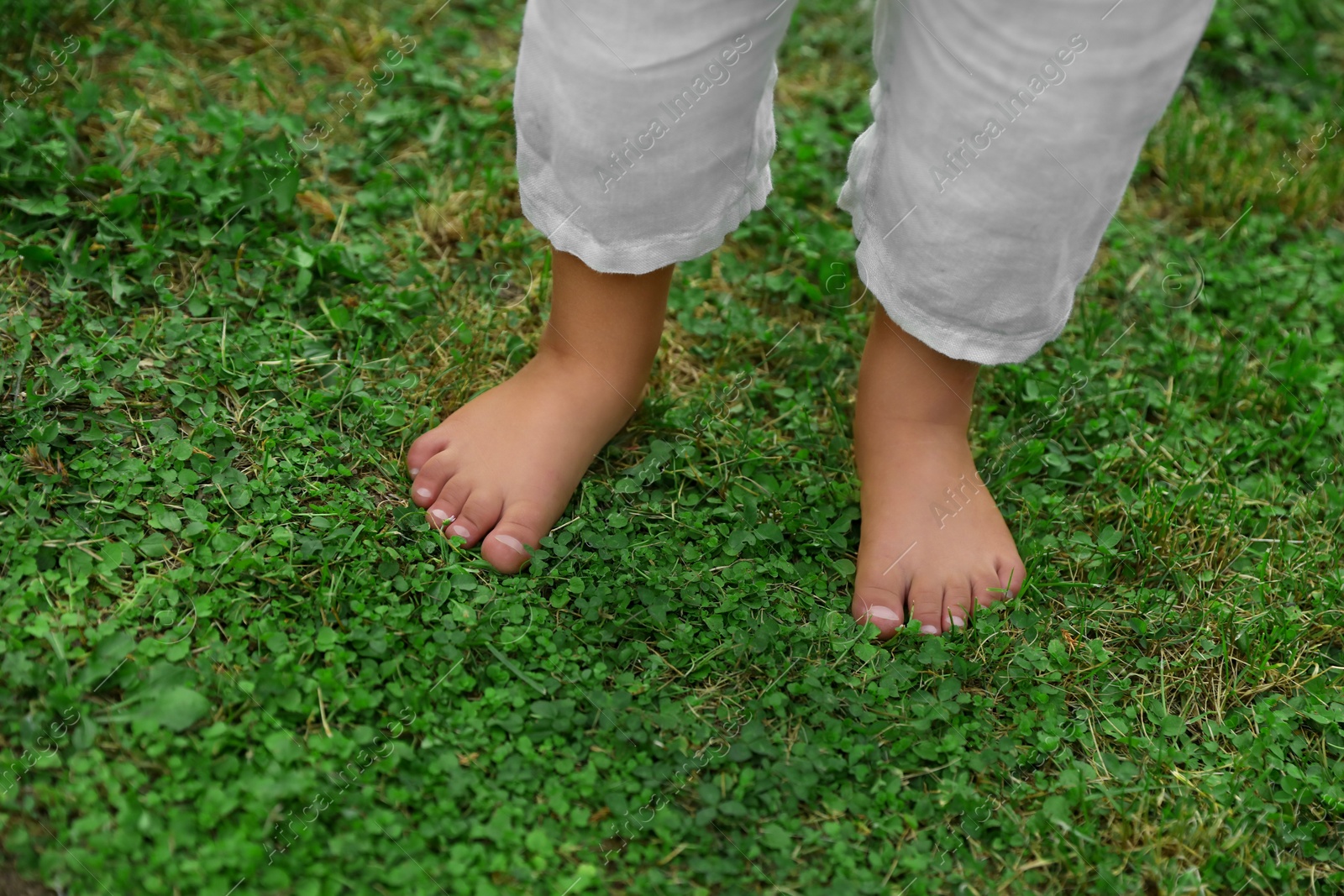 Photo of Little child standing barefoot on green grass outdoors, closeup. Enjoying nature