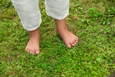 Little child standing barefoot on green grass outdoors, closeup. Enjoying nature