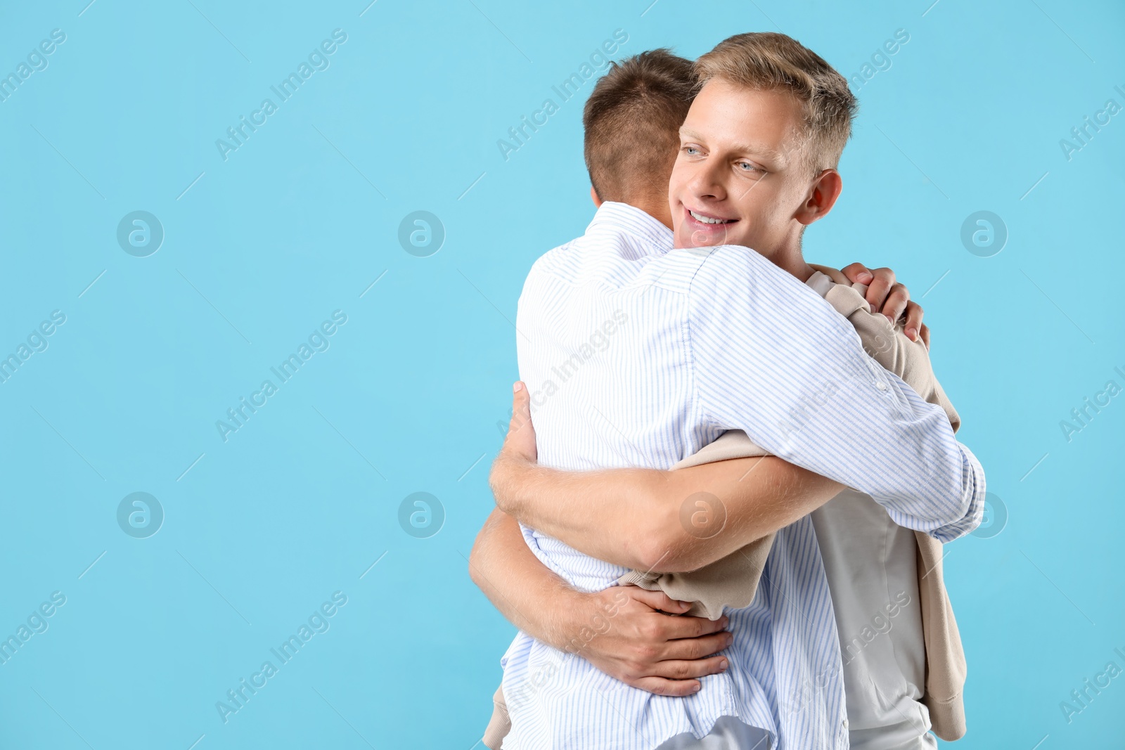 Photo of Two brothers hugging on light blue background. Space for text