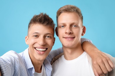 Happy brothers taking selfie on light blue background