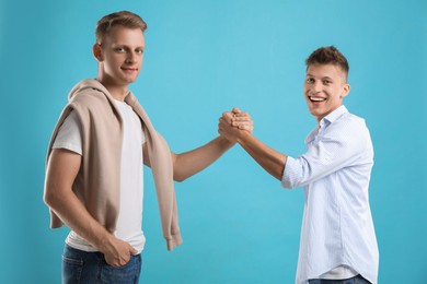 Happy brothers clasping hands on light blue background