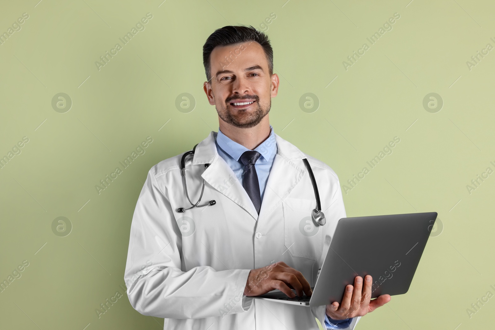 Photo of Smiling doctor with stethoscope using laptop on olive background