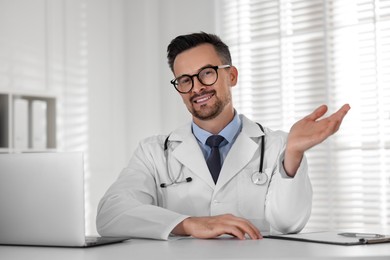 Photo of Smiling doctor working with laptop at table in clinic