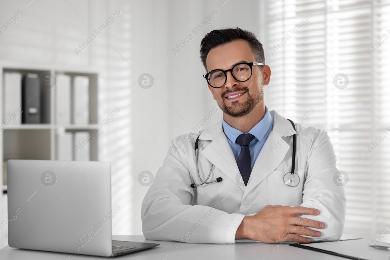 Photo of Smiling doctor working with laptop at table in clinic