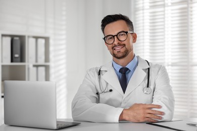 Smiling doctor working with laptop at table in clinic