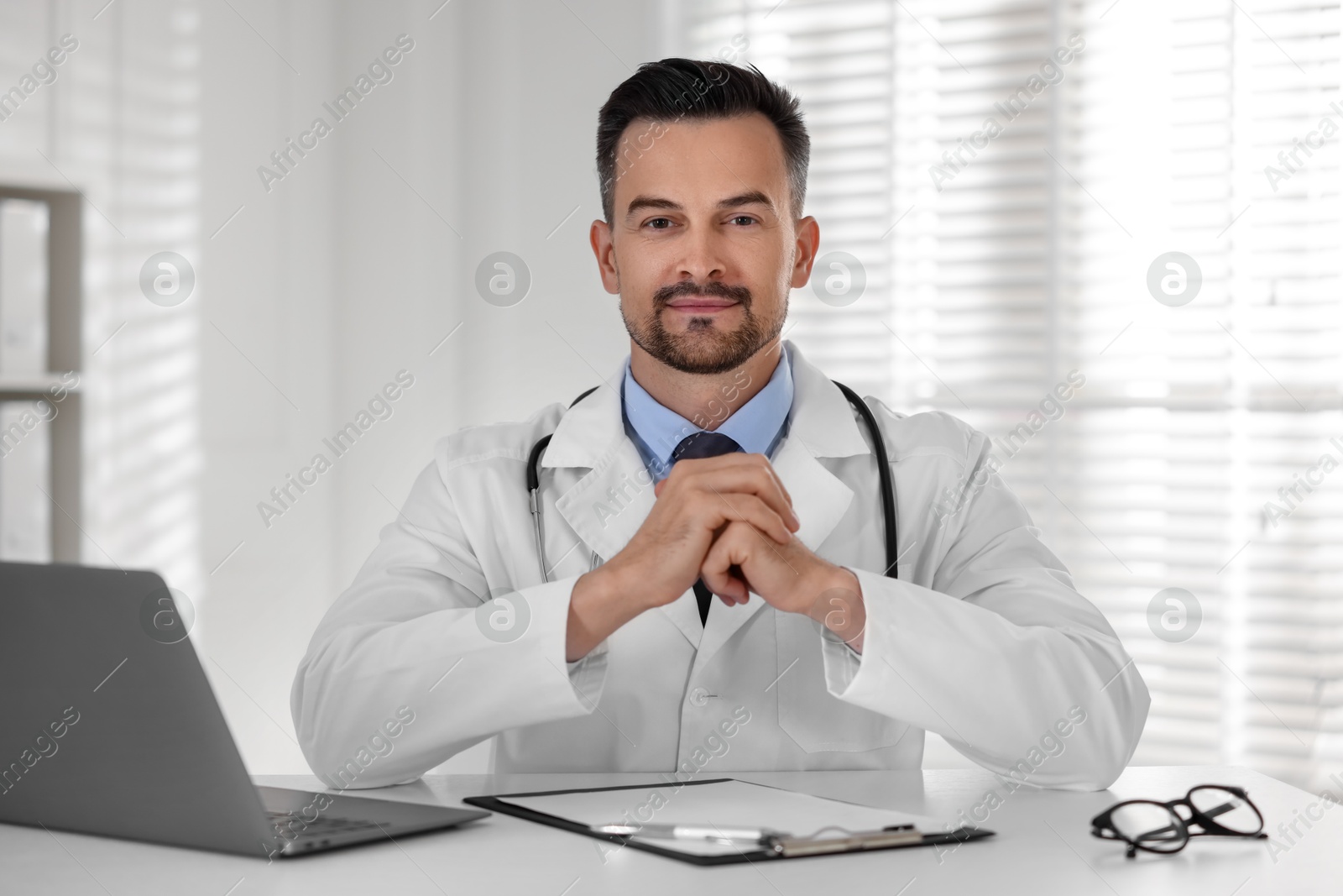 Photo of Doctor with clipboard and laptop at table in clinic