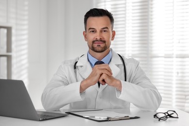 Doctor with clipboard and laptop at table in clinic