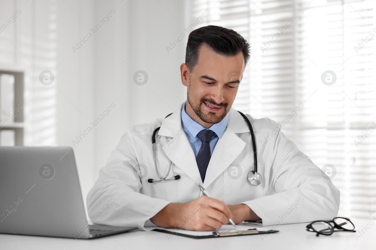 Photo of Smiling doctor working at table in clinic