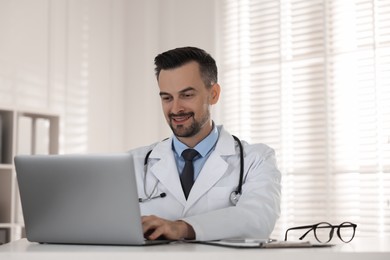 Photo of Smiling doctor working with laptop at table in clinic