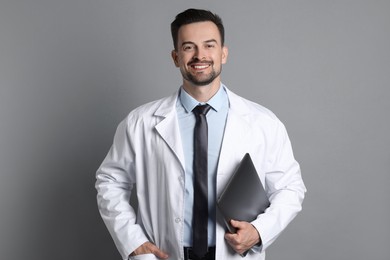 Smiling doctor with laptop on grey background