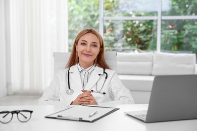 Photo of Doctor with stethoscope, laptop and clipboard at table in clinic