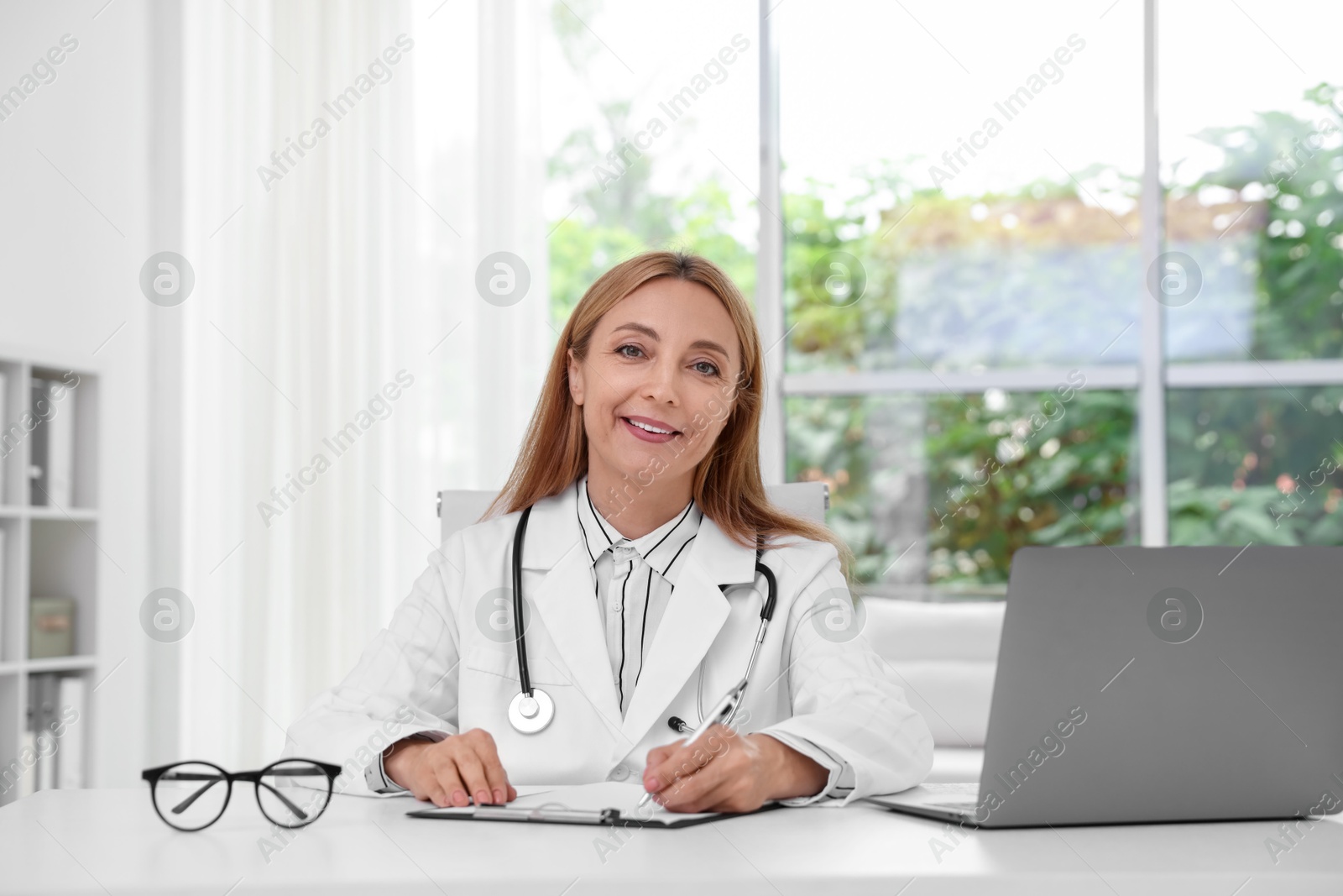 Photo of Doctor with stethoscope, laptop and clipboard at table in clinic