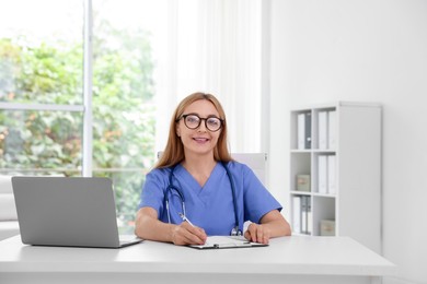 Photo of Doctor with stethoscope, laptop and clipboard at table in clinic