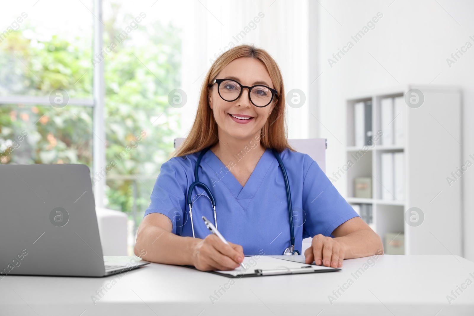 Photo of Doctor with stethoscope, laptop and clipboard at table in clinic