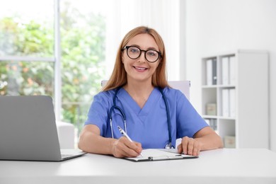 Doctor with stethoscope, laptop and clipboard at table in clinic