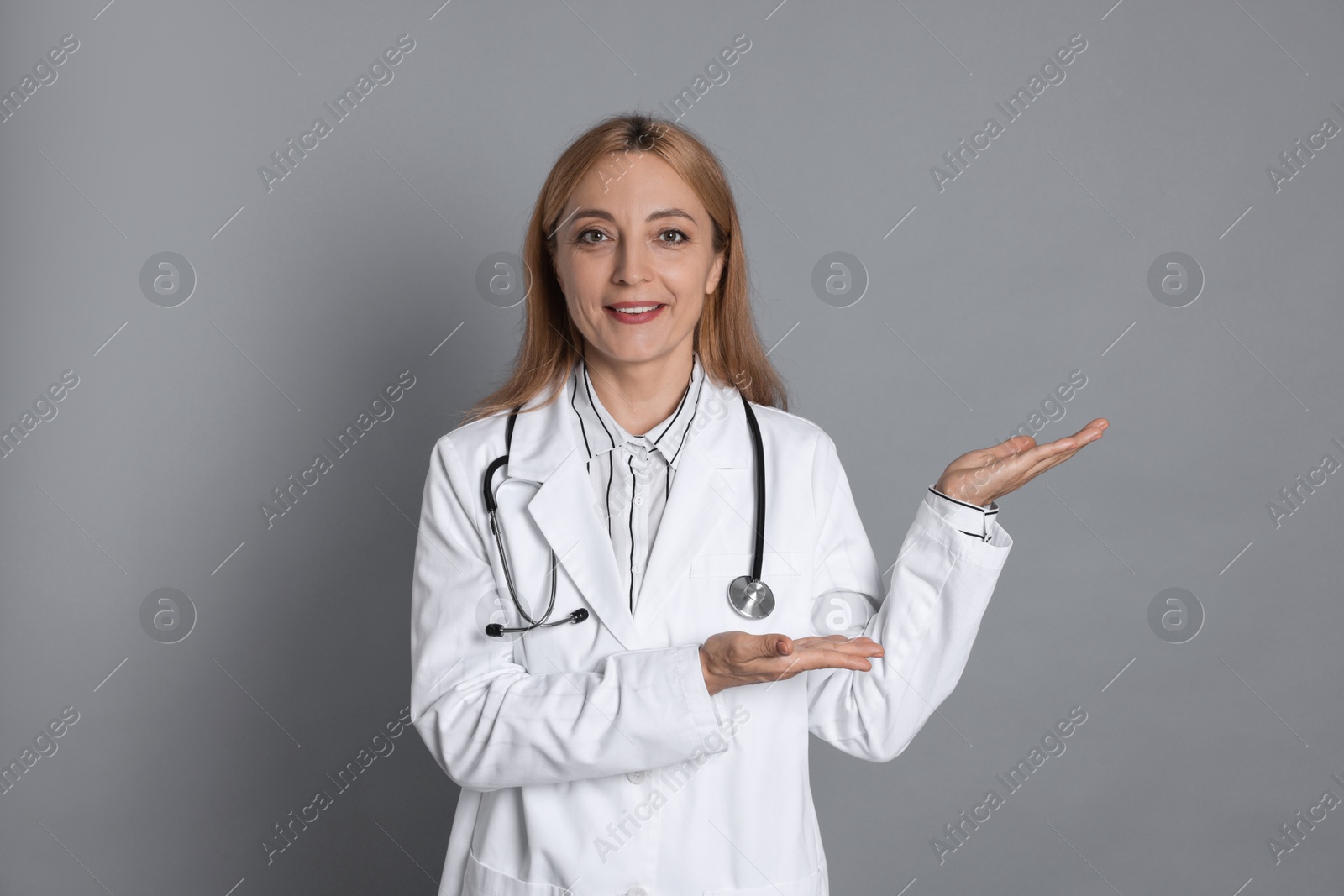 Photo of Doctor with stethoscope showing something on gray background