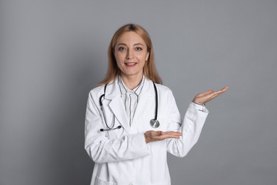 Doctor with stethoscope showing something on gray background