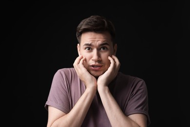 Portrait of scared young man on black background