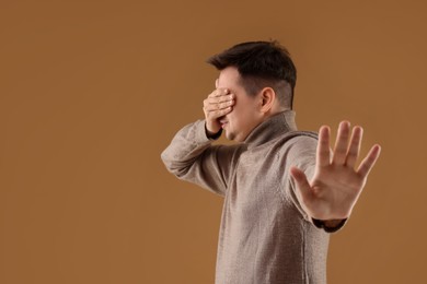 Portrait of scared young man on brown background, space for text