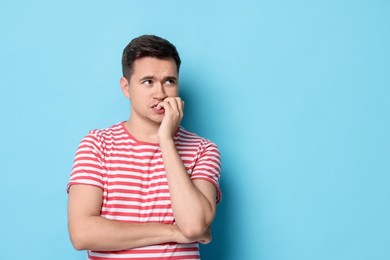 Portrait of scared young man on light blue background, space for text