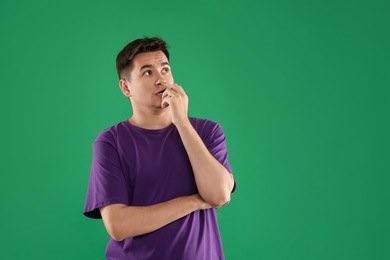 Portrait of scared young man on green background, space for text