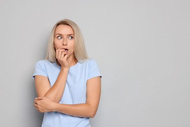 Portrait of scared woman on gray background, space for text