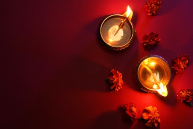 Photo of Diwali celebration. Diya lamps and beautiful flowers on red background, flat lay. Space for text