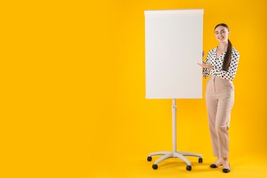 Photo of Happy woman near flip chart on orange background. Mockup for design