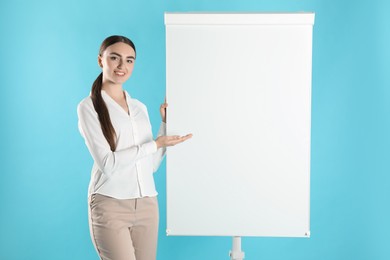 Photo of Happy woman near flip chart on light blue background. Mockup for design