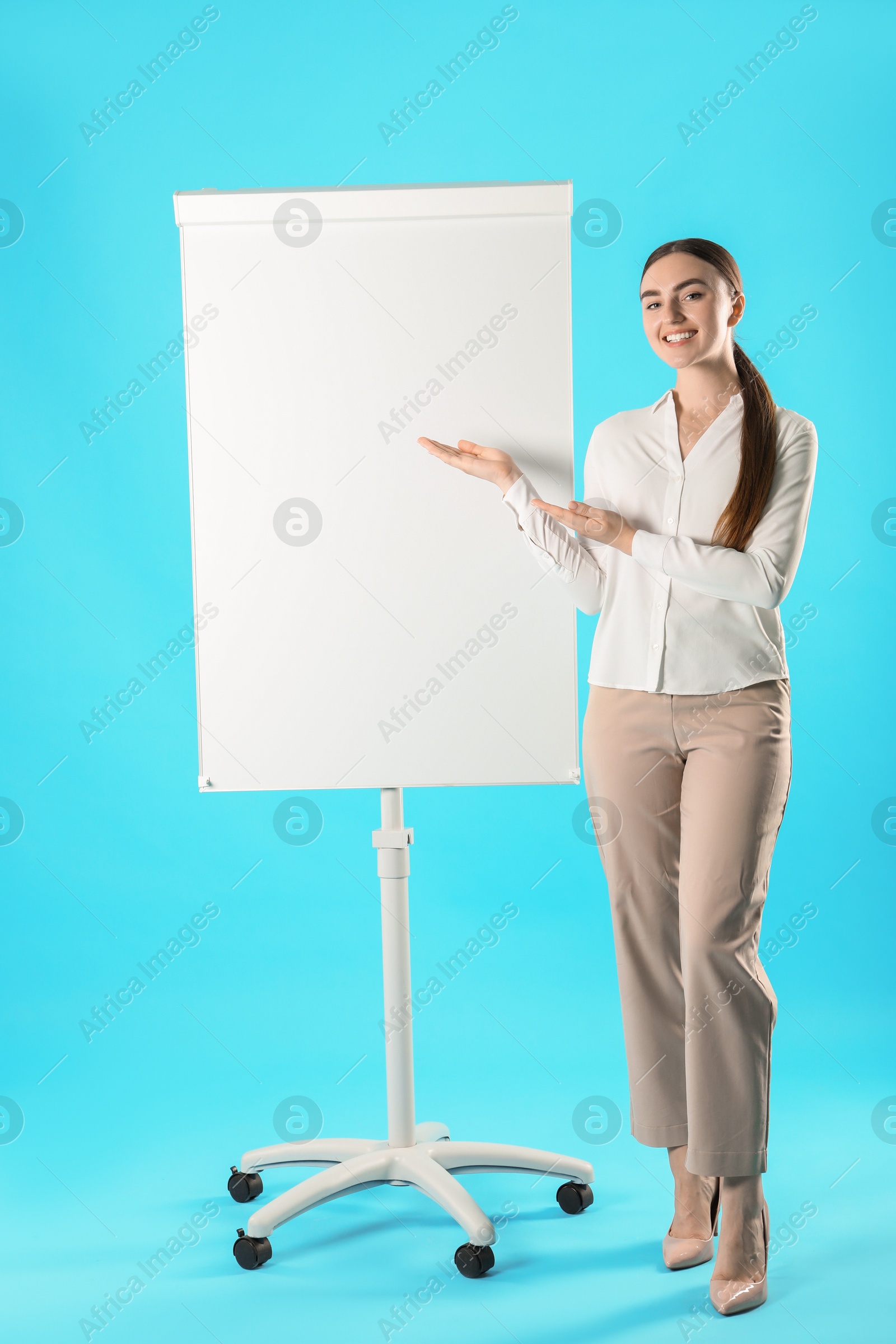 Photo of Happy woman near flip chart on light blue background. Mockup for design