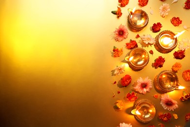 Photo of Diwali celebration. Diya lamps and beautiful flowers on golden background, flat lay. Space for text