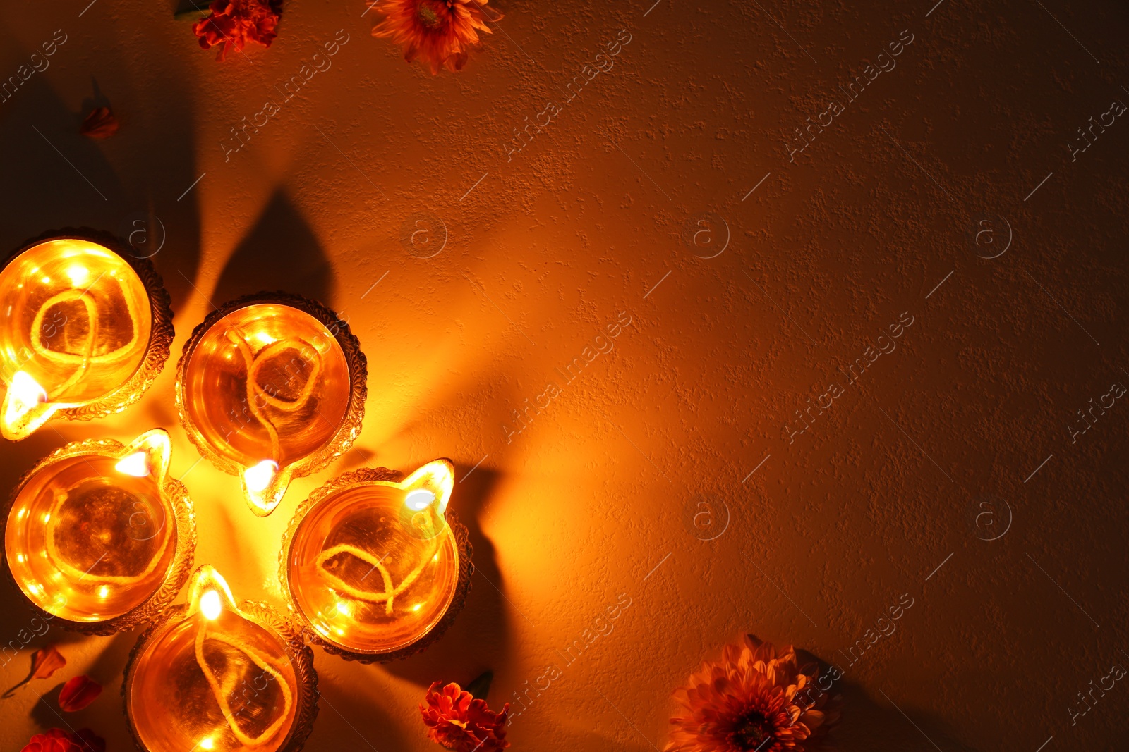 Photo of Diwali celebration. Diya lamps and beautiful flowers on dark textured surface, flat lay. Space for text