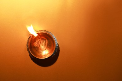 Photo of Diwali celebration. Diya lamp on orange background, top view. Space for text