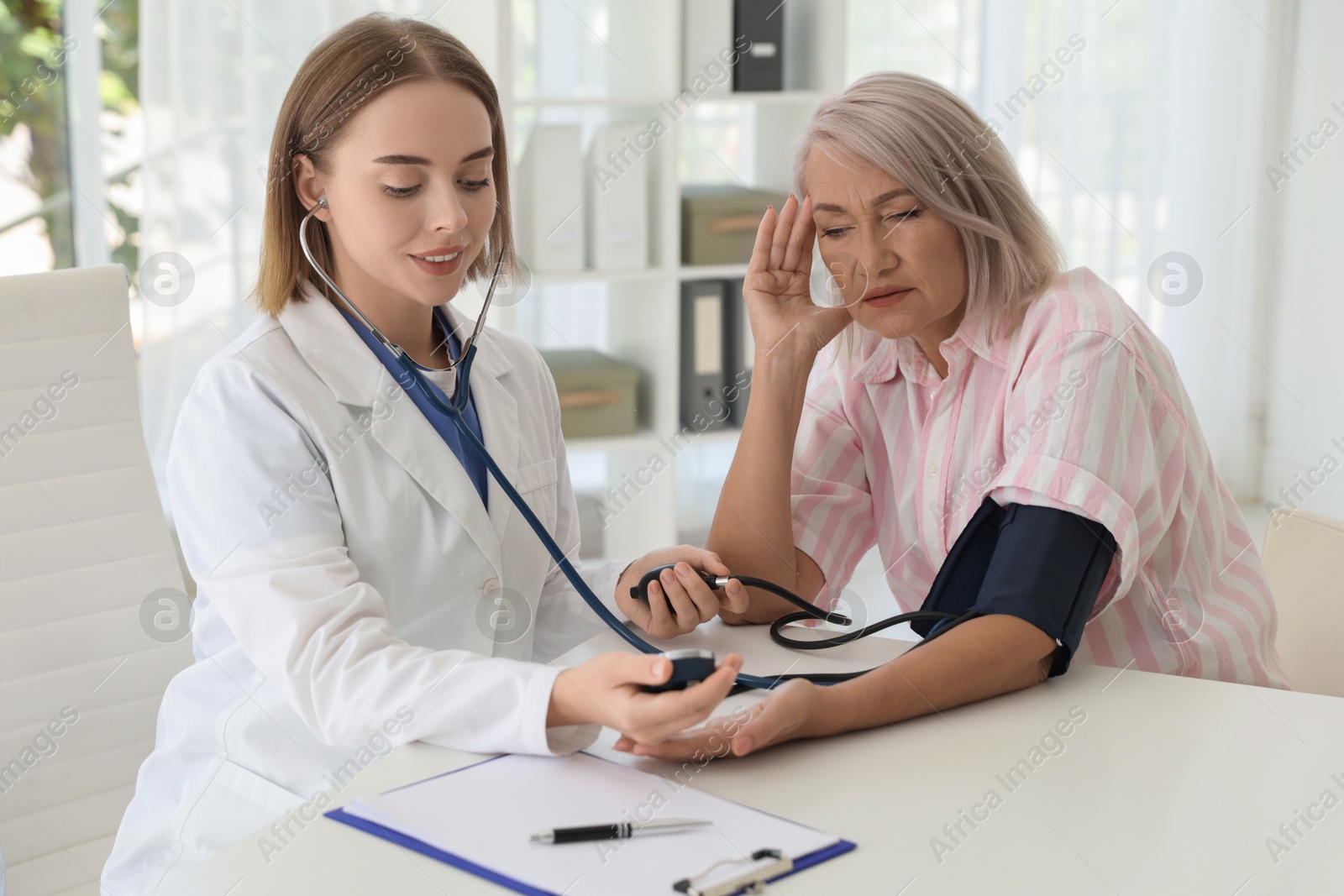 Photo of Doctor measuring patient's blood pressure at table in hospital