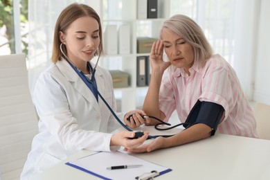 Doctor measuring patient's blood pressure at table in hospital