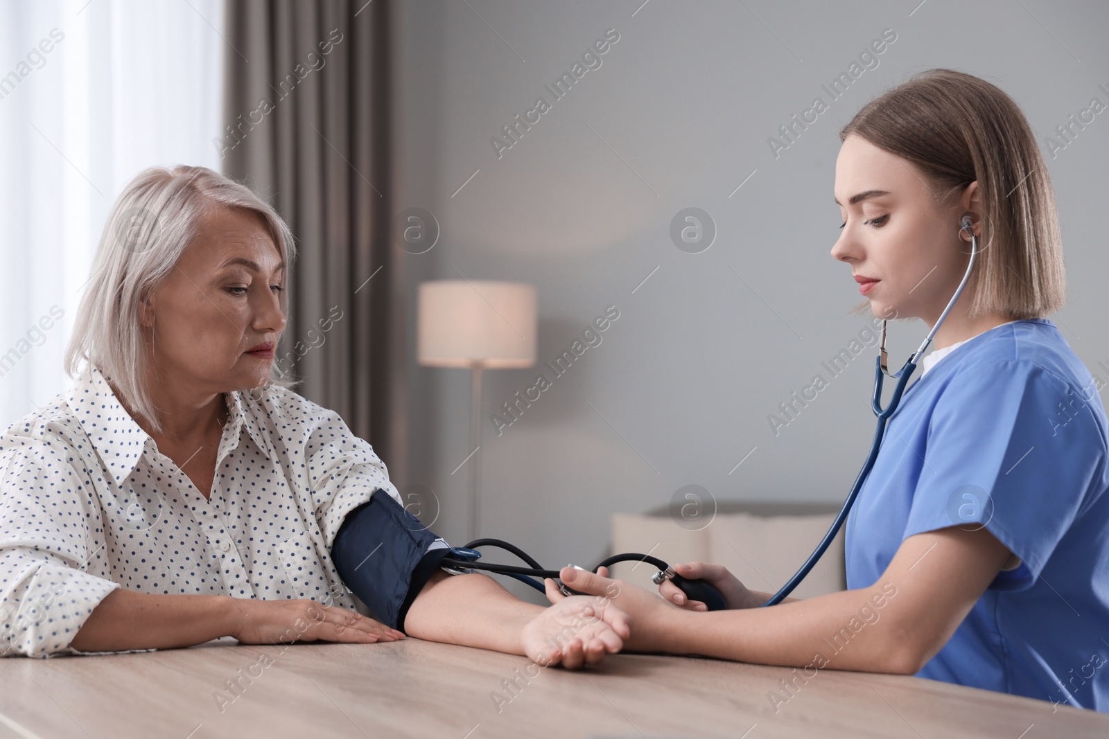 Photo of Healthcare worker measuring patient's blood pressure at wooden table indoors