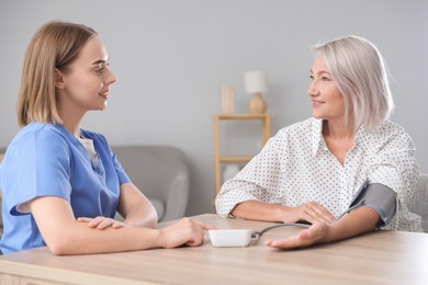 Healthcare worker measuring patient's blood pressure at wooden table indoors