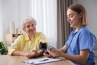 Healthcare worker measuring patient's blood pressure at wooden table indoors