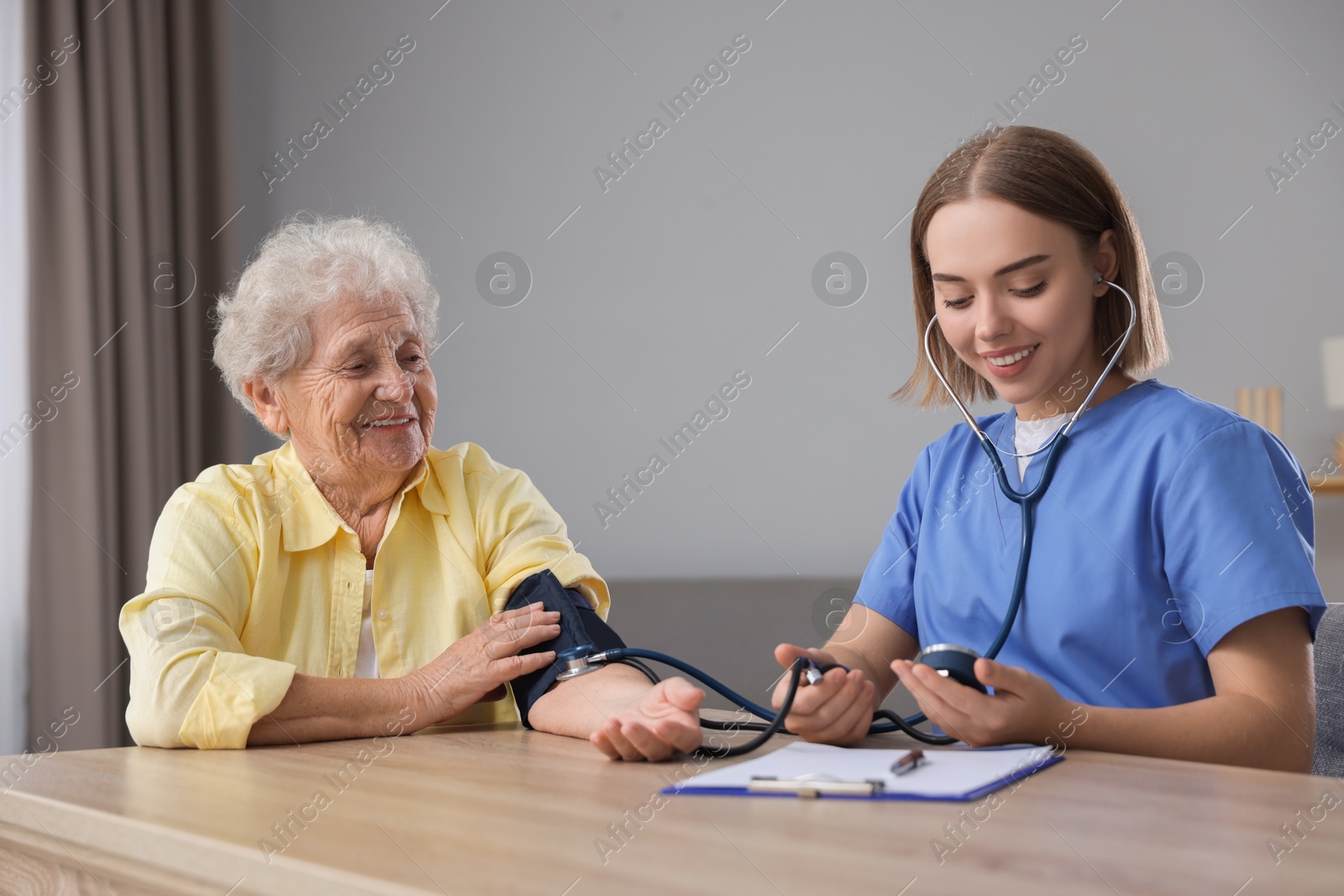 Photo of Healthcare worker measuring patient's blood pressure at wooden table indoors