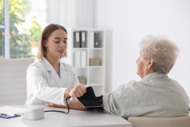 Doctor measuring patient's blood pressure at table in hospital