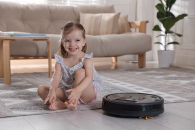 Cute little girl with robotic vacuum cleaner on floor at home