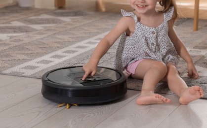 Photo of Little girl with robotic vacuum cleaner on floor at home, closeup