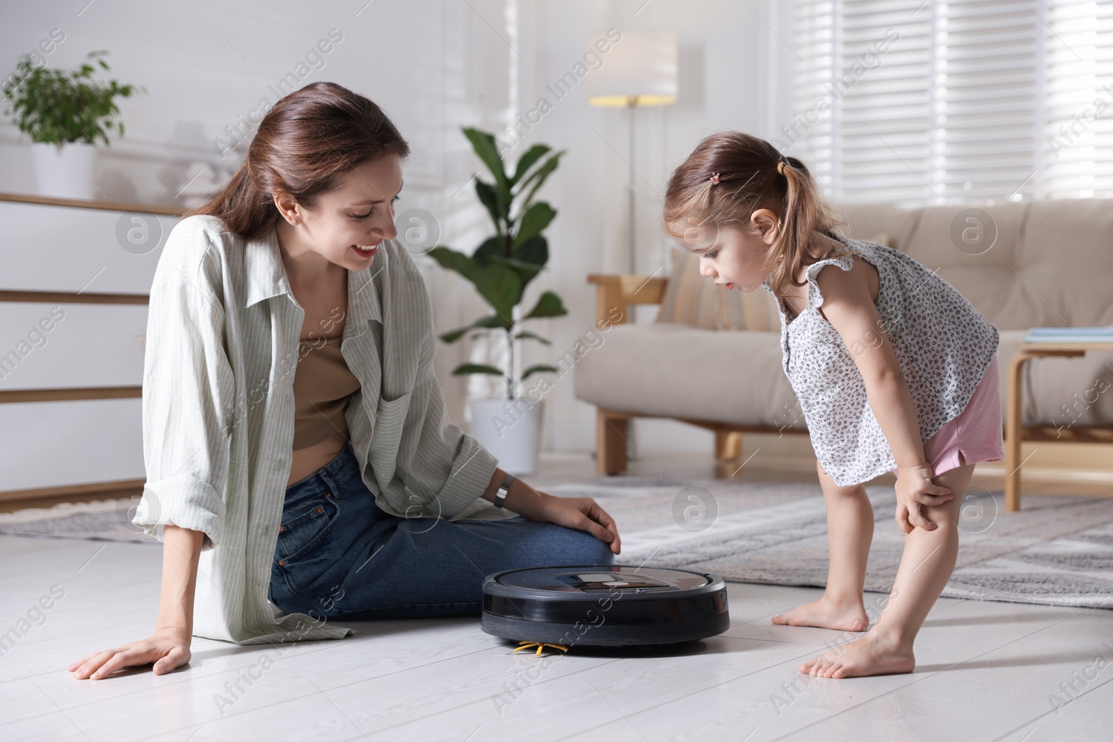 Photo of Mother and her daughter with robotic vacuum cleaner at home