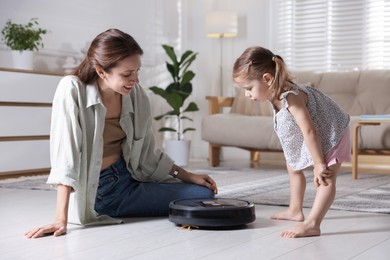 Mother and her daughter with robotic vacuum cleaner at home