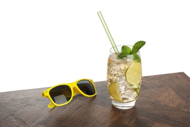 Photo of Glass of tasty refreshing drink, straw and sunglasses on wooden table against white background