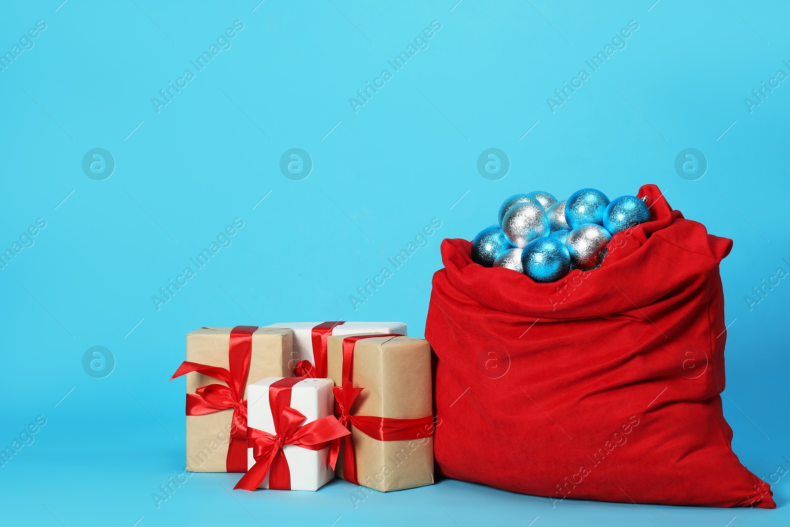 Photo of Santa Claus bag with baubles and gift boxes on light blue background, space for text