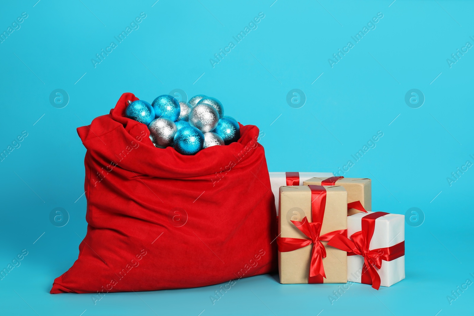 Photo of Santa Claus bag with baubles and gift boxes on light blue background