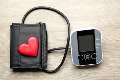 Photo of Blood pressure measuring device and heart figure on wooden table, top view