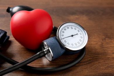 Blood pressure measuring device and squeeze heart on wooden table, closeup