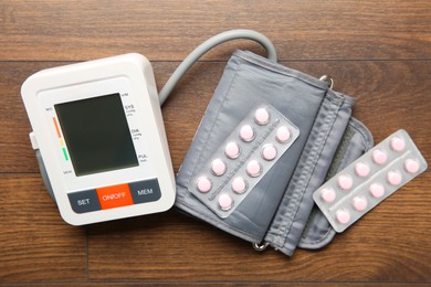 Blood pressure measuring device and pills on wooden table, top view